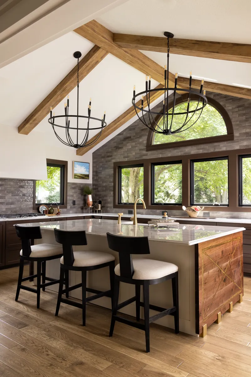 This kitchen features rustic faux wood ceiling beams, a tiled accent wall, and a luxurious marble island with modern counter stools, creating an inviting contemporary design.