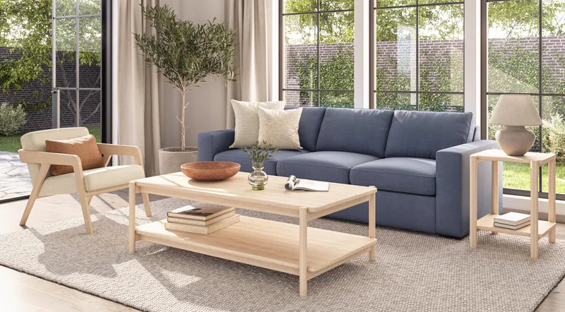 This inviting modern living space features a blue natural fiber sofa, light wood furniture, textured cushions, and a woven rug, bathed in natural light from large windows.