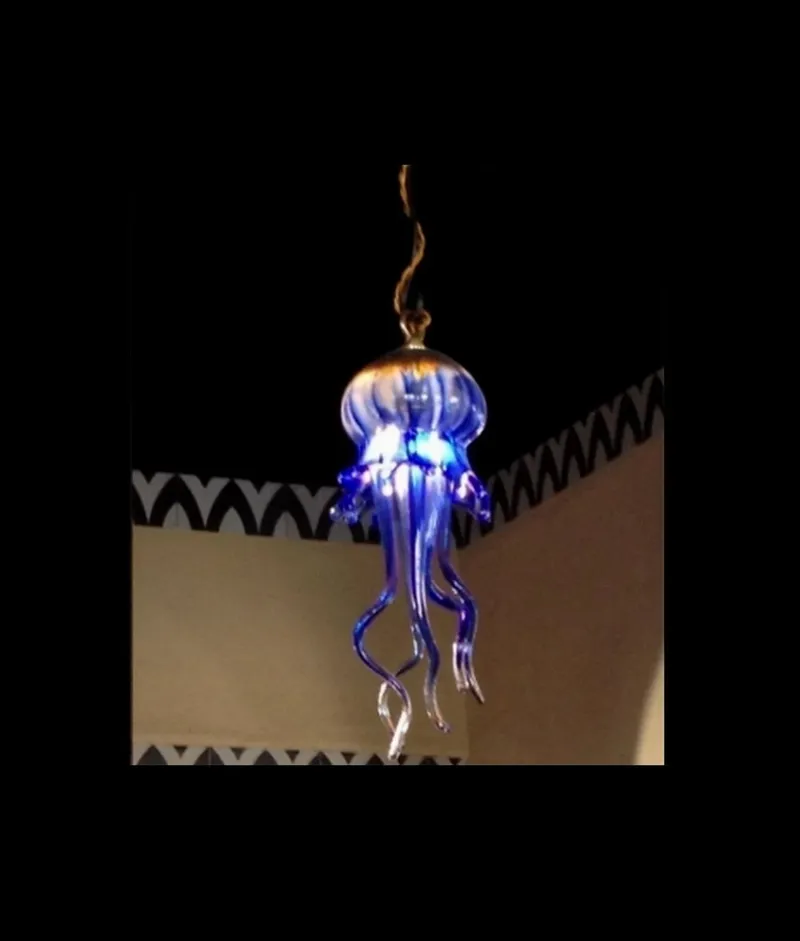 A mesmerizing glass jellyfish chandelier with glowing blue accents illuminates a contemporary interior, contrasting with the dark background and patterned wall decor.