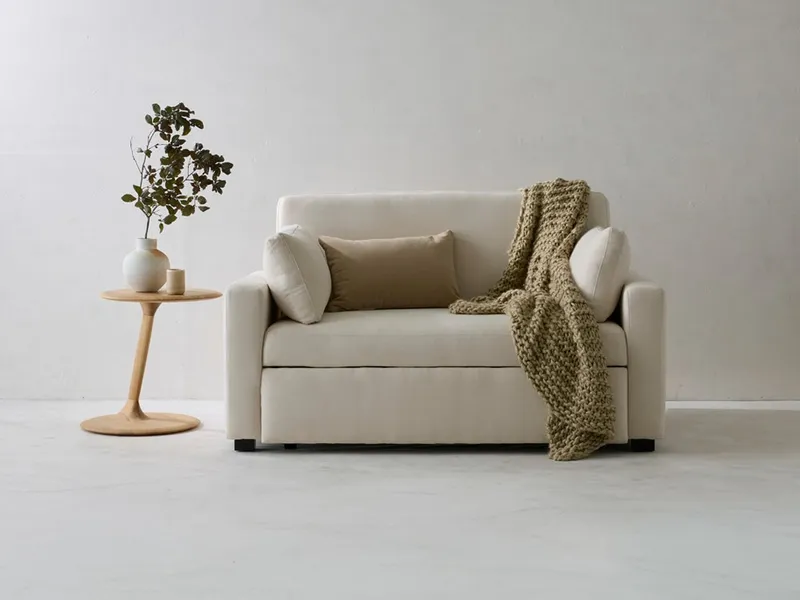 A minimalist modern interior features a cream eco-friendly natural fiber sofa, accented by a chunky knit throw, a wooden side table, and subtle organic decor.