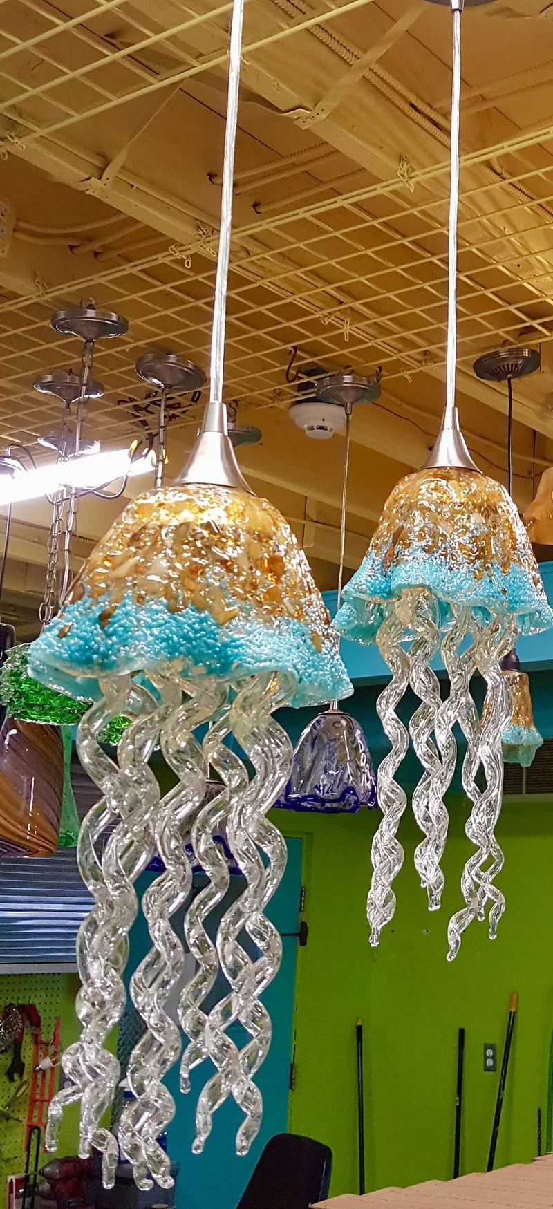 Two exquisite glass jellyfish pendant lights, with textured golden and turquoise caps and swirling clear glass tentacles, create a vibrant lighting design.