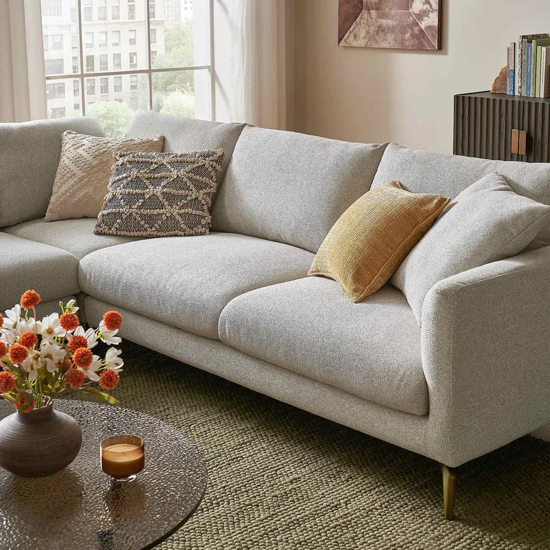 A contemporary living room showcases a light natural fiber upholstered sectional sofa with textured throw pillows, a glass coffee table, and an inviting braided rug.