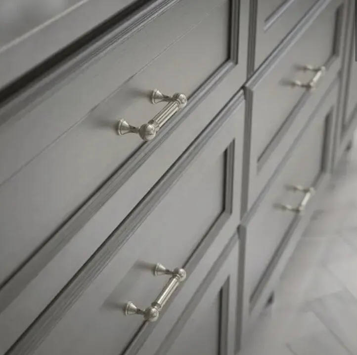 Close-up of sleek brushed nickel pulls on classic gray shaker-style kitchen cabinetry, showcasing detailed hardware against a soft, refined interior design.