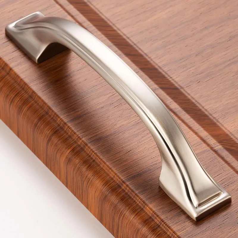 A sleek satin nickel kitchen cabinet pull with refined detailing rests elegantly on a warm, richly grained wooden surface, showcasing modern interior design hardware.