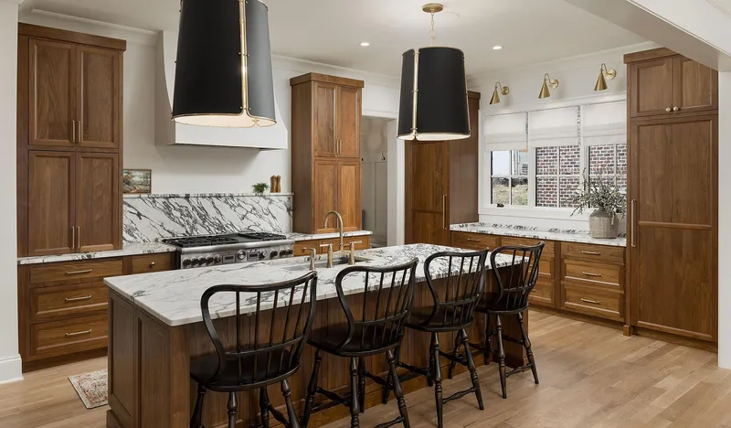 This elegant kitchen features warm stained wood cabinetry, a striking marble backsplash and countertops, and a functional island with stylish seating and ample storage.