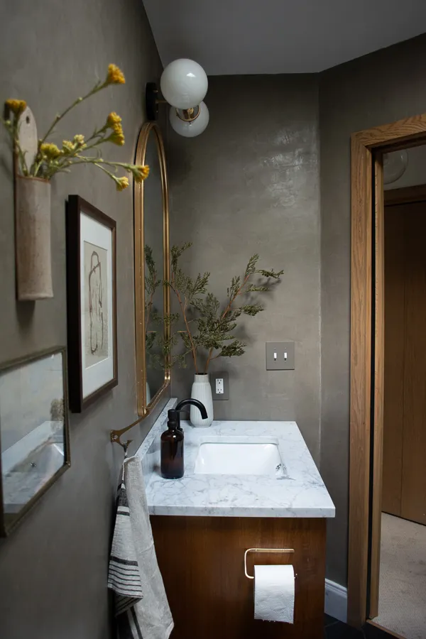 A chic powder room features a smooth clay-based wall finish, a luxurious marble vanity, and a warm wooden cabinet, creating a sophisticated and textured modern interior.